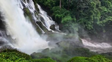 Yağmur mevsiminde yemyeşil bir ormanda çağlayan güçlü bir şelale. Nehir akıntısı güçlüdür ve şiddetli yağıştan sonra su çamurlu hale gelir. Bu da doğanın ham enerjisini gösterir.