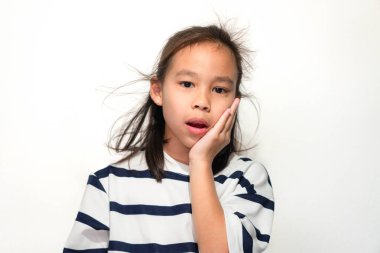 Şaşırmış bir Asyalı kız tek eliyle yanağına dokunuyor, çizgili bir gömlek giyiyor ve beyaz bir arka plana karşı hayret verici bir ifade sergiliyor..