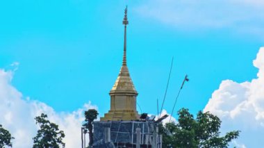 Gökyüzünde hareket eden dinamik bulutların olduğu bir dağın tepesindeki altın bir pagoda 'nın hızlandırılmış görüntüleri, Tayland' daki maneviyatı, Budizmi ve doğal güzelliği simgeliyor..