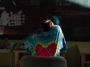 Asyalı liseli kız pencerenin yanındaki çalışma masasında tek başına oturuyor ve güneş ışığı parlıyor. Yalnızlığı, eğitimi, konsantrasyonu ve kapalı alanda öğrenim ve öğrenim yaşam tarzını temsil eder..