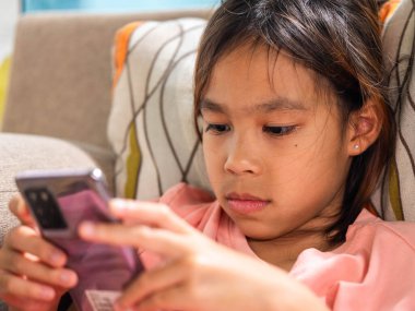 Ciddi ve odaklanmış bir ifadeyle akıllı telefon kullanan genç bir kız. Fotoğraf dijital eğitim, mobil yaşam tarzı ve modern çocukluğu temsil etmektedir..