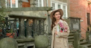 Şehir binalarında telefon kullanırken yürürken sevimli çekici bir kadın etrafına bakıyor güneş ışığında mutlu bir gülücük atıyor. Portre, genç, internet, cep telefonu, sokak, güzel, seyahat, mobil, şık. Yavaş