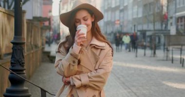 Şehir binalarında telefon kullanırken yürürken sevimli çekici bir kadın etrafına bakıyor güneş ışığında mutlu bir gülücük atıyor. Portre, genç, internet, cep telefonu, sokak, güzel, seyahat, mobil, şık. Yavaş