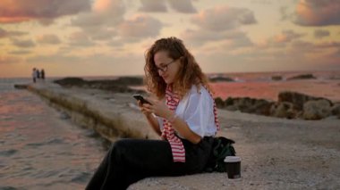 Beautiful young european women girl by the sea, takes a selfie and photographs the sunset. 