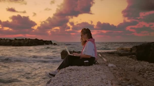 在海边工作的年轻的欧洲女人 在日落的背景下带着笔记本电脑工作 — 图库视频影像