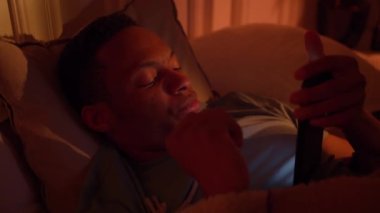 Insomnia night Dark-skinned guy Tired disturbed with anxiety trying to rest in bed with phone.