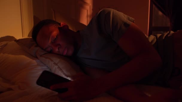 不眠症の夜暗い肌の男疲れを乱すで不安で休息しようとしているベッドで電話 — ストック動画