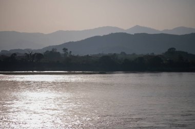 Mekong Nehri 'nin çevresi dağlarla çevrili ve gün batımında sarı güneş ışınlarıyla çevrili. Chiang Khong, Chiang Rai, Kuzey Tayland.