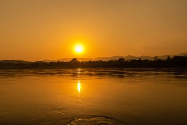 Mekong Nehri 'nin çevresi dağlarla çevrili ve gün batımında sarı güneş ışınlarıyla çevrili. Chiang Khong, Chiang Rai, Kuzey Tayland.