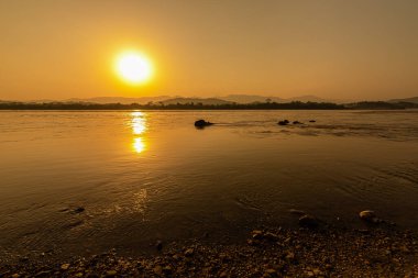 Mekong Nehri 'nin çevresi dağlarla çevrili ve gün batımında sarı güneş ışınlarıyla çevrili. Chiang Khong, Chiang Rai, Kuzey Tayland.