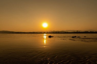 Mekong Nehri 'nin çevresi dağlarla çevrili ve gün batımında sarı güneş ışınlarıyla çevrili. Chiang Khong, Chiang Rai, Kuzey Tayland.