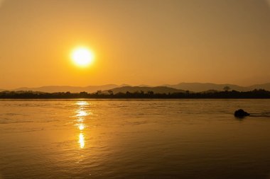 Mekong Nehri 'nin çevresi dağlarla çevrili ve gün batımında sarı güneş ışınlarıyla çevrili. Chiang Khong, Chiang Rai, Kuzey Tayland.