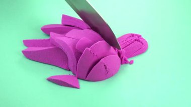 Çok renkli bir arka planda, kinetik kumu bıçakla kesmek.