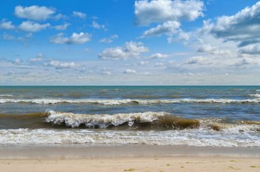 Deniz dalgaları sahili mavi gökyüzüne karşı yıkıyor. Vahşi bir sahilde manzara. Yazın deniz..
