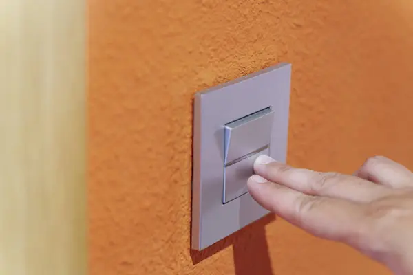 Close-up of hand pressing a grey light button on orange wall