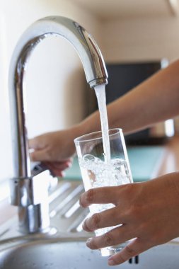 Mutfak musluğunda bir bardak soğuk su dolduran kadın.