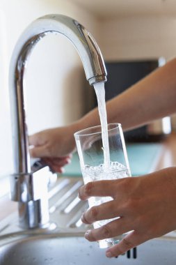 Mutfak musluğunda bir bardak soğuk su dolduran kadın.