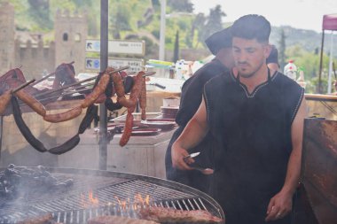 Kalabalık bir ortaçağ pazarında büyük bir ızgarada cızırdayan etler eski aşçılık geleneklerinin özünü yakalıyor.