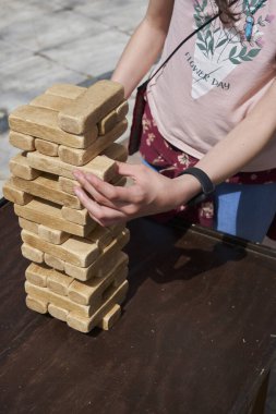 A person skillfully removing a block from a giant wooden Jenga tower outdoors clipart