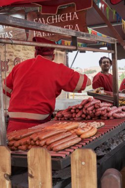 Ortaçağ pazarında açık havada çeşitli sosisleri ızgara yapan işçilerle dolu hareketli bir yiyecek tezgahı.