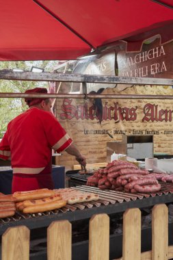 Ortaçağ pazarında açık havada çeşitli sosisleri ızgara yapan işçilerle dolu hareketli bir yiyecek tezgahı.