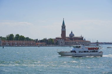 Venedik şehir manzarasında kanalda bir tekne ve arka planda tarihi bir çan kulesi var.