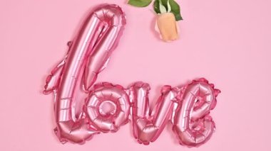 Romantic Valentine's day greeting card with Love balloon and romantic natural roses on pastel pink background. Flat lay. Stop motion