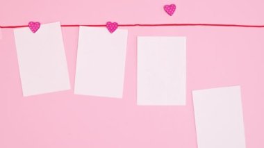 Copy space papers hanged on red rope on pastel pink background. Valentine's day greeting card. Stop motion. Flat lay