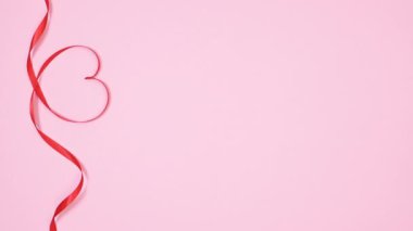 Romantic ribbons make hearts shapes on pastel pink background. Vertical stop motion copy space. Flat lay