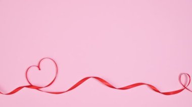 Romantic ribbons make hearts shapes on pastel pink background. Copy space flat lay. Stop motion