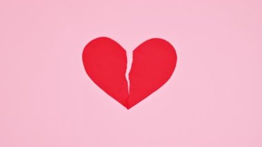 Breaking heart in two pieces on pastel pink background. Flat lay. Stop motion