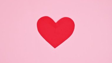 Two pieces of heart connecting in one on pastel pink background. Flat lay. Stop motion