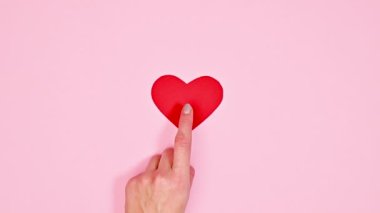 Hand touching red heart on pastel pink background. Valentine's day stop motion. Flat lay