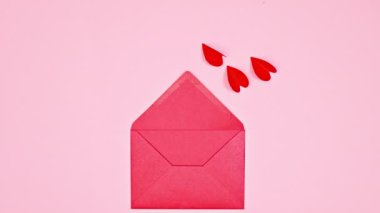 Flying hearts with wings enter in red envelope on pastel pink background. Flat lay. Stop motion