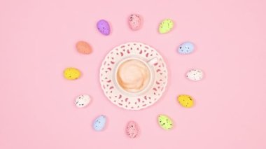 Cup of espresso coffee spin in circle with Easter eggs on pastel pink background. Flat lay. Stop motion