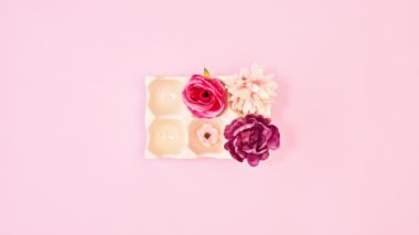 Growing flowers from ceramic Easter bowl for eggs on pastel pink background. Stop motion flat lay