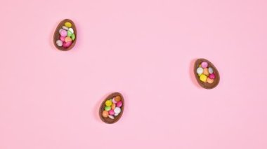 Creative Easter pattern with chocolate eggs, rabbits and carrots appear on pastel pink background. Flat lay. Stop motion