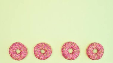 Strawberry glazed donuts spin in circle on bottom of light green background. Copy space sweet food concept. Stop motion. Flat lay