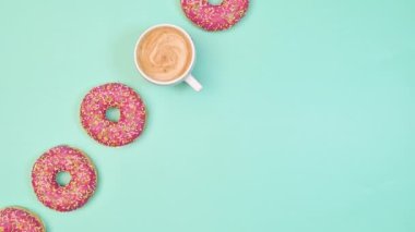 Sweet strawberry glazed donuts and cup of espresso coffee appear on pastel blue copy space background. Flat lay. Food concept. Stop motion