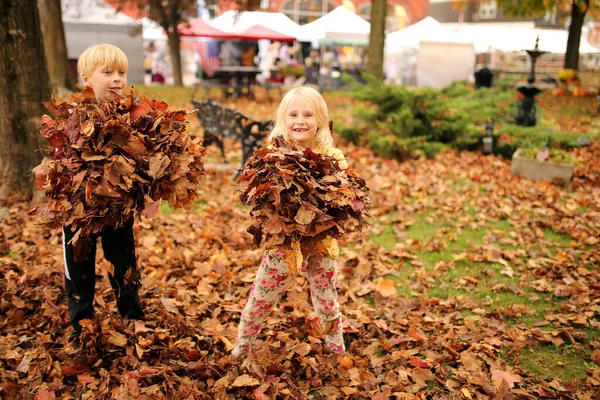 小さな町の秋祭りでの秋のオークの葉の遊びとして2人の幸せな小さな子供たちが笑っています — ストック写真