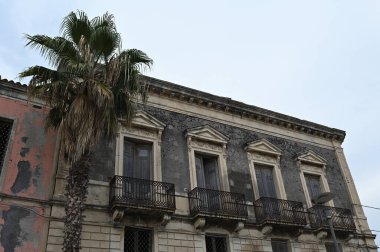 Büyüleyici binalar, geleneksel mimarinin sergilendiği Giarre, Sicilya sokaklarına dizilmiştir. Sahne, sıcak Akdeniz güneşinin altında kasabanın hayat dolu yaşamını yakalıyor..