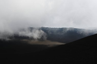 Etna Dağı 'ndaki bir volkanik sırtın silueti. Sicilya, Etna Dağı 'ndaki volkanik bir sırtın dramatik bir silueti. Bulutlu gökyüzünde tek başına görünen bir figür.. 