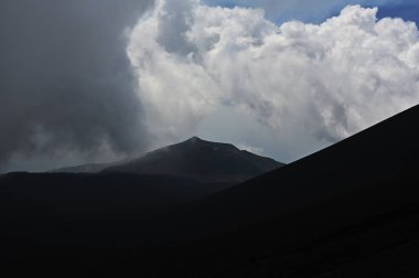 Etna Dağı 'ndaki bir volkanik sırtın silueti. Sicilya, Etna Dağı 'ndaki volkanik bir sırtın dramatik bir silueti. Bulutlu gökyüzünde tek başına görünen bir figür.. 