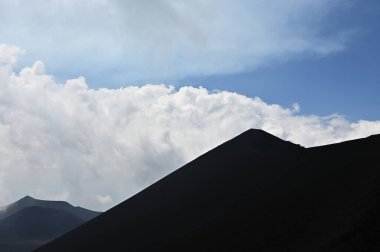 Etna Dağı 'ndaki bir volkanik sırtın silueti. Sicilya, Etna Dağı 'ndaki volkanik bir sırtın dramatik bir silueti. Bulutlu gökyüzünde tek başına görünen bir figür.. 