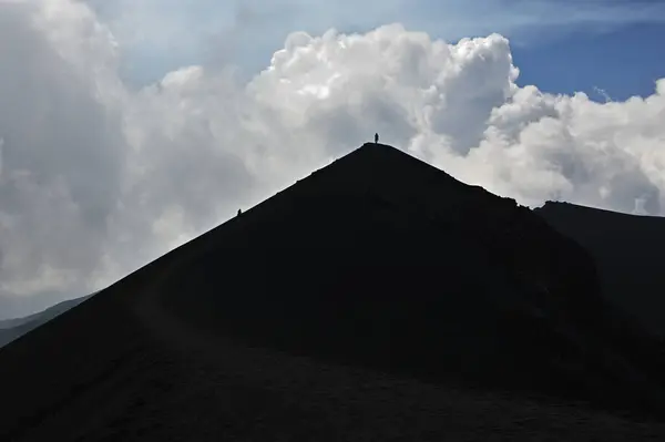 Etna Dağı 'ndaki bir volkanik sırtın silueti. Sicilya, Etna Dağı 'ndaki volkanik bir sırtın dramatik bir silueti. Bulutlu gökyüzünde tek başına görünen bir figür.. 