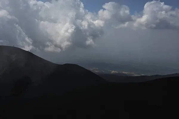 Etna Dağı 'ndaki bir volkanik sırtın silueti. Sicilya, Etna Dağı 'ndaki volkanik bir sırtın dramatik bir silueti. Bulutlu gökyüzünde tek başına görünen bir figür.. 