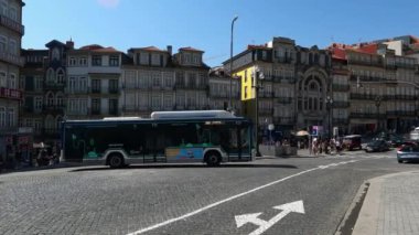 Porto, Portekiz 'de So Bento Caddesi' nin ortasındaki bir sokak köşesinden geçen otobüs, araba ve motorsikletin 4K videosu güneşli bir günde kalabalığın yanından geçerken..