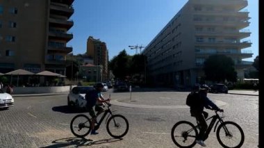 İnsanlar otomobil ve otobüslerin yanında bisiklet sürerken şehir merkezindeki hareketli bir bölgenin enerjisini yakalayın. Bu dinamik görüntüler şehir yaşamını gösteriyor, kalabalık bir caddede bisikletçiler ve araçların birlikte yaşadıklarını vurguluyor..