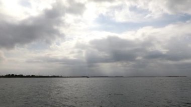 Tepemizde şiddetli bulutlar belirdi ve dramatik bir atmosfer yarattı. Arka planda, şehrin ufuk çizgisi görülebiliyor ve doğal manzaraya bir şehir kontrastı ekleniyor. Dengesiz hava ve dinamik okyanus dalgaları bir yoğunluk ve beklenti hissi verir..