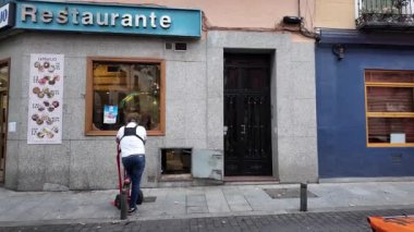 Çalışan bir yükleyici büyüleyici bir İspanyol restoranının önünde sabırla duruyor, hareketli bir şehir ortamında günlük hayatın ritmini somutlaştırıyor. Günlük anları, şehir kültürünü veya iş hayatı görüntülerini gösteren projeler için idealdir.. 